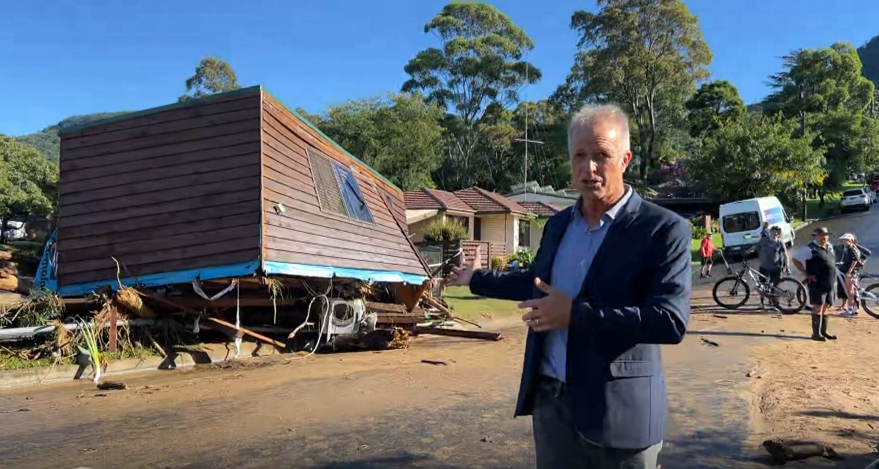 A man stands next to a wooden building with a sloping wall.