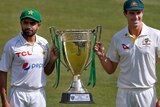 Babar Azam and Pat Cummins, wearing whites, smile while holding a large trophy together