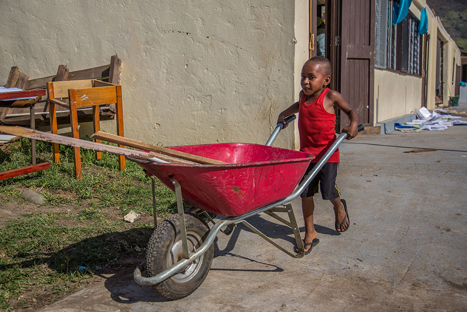 A little boy pushes a wheelbarrow to help with his school's clean up