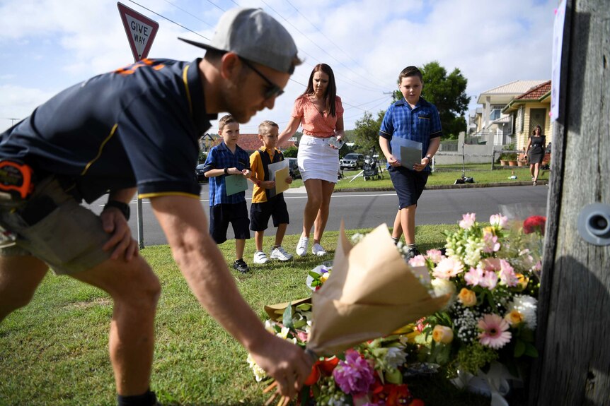 A man lays flowers on the footpath as a part of a tribute to the Baxter family.