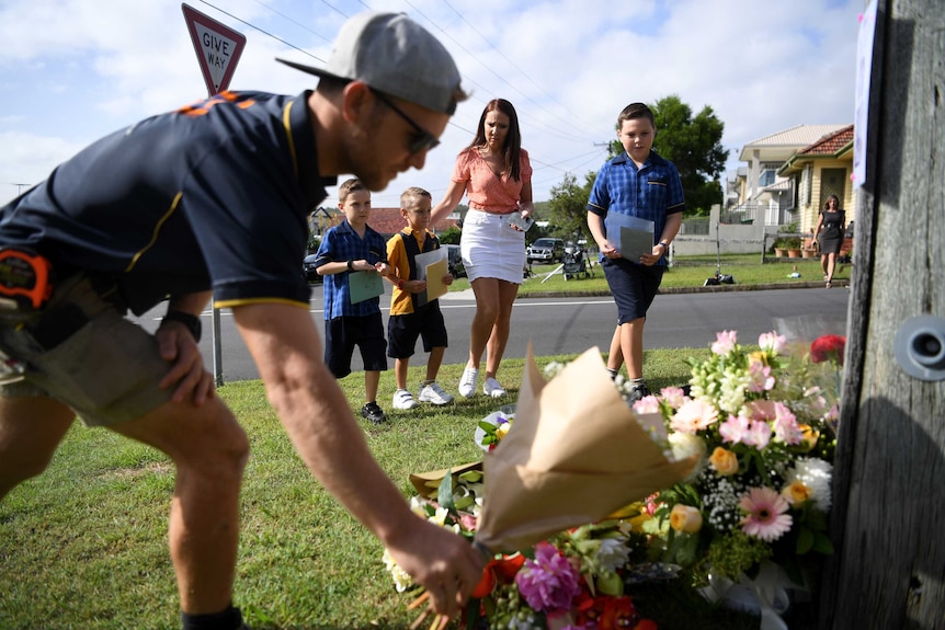 A man lays flowers on the footpath as a part of a tribute to the Baxter family.