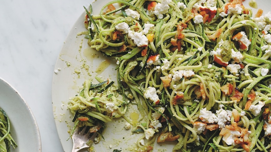 Courgetti pasta with pistachio, green herbs and ricotta on a plate with fork.