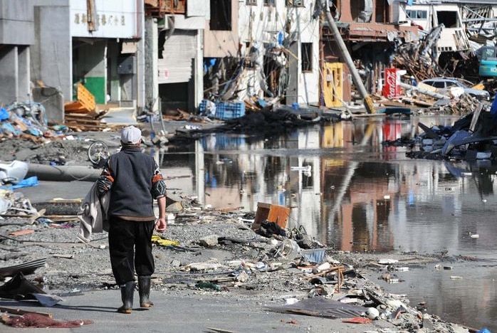 A man walks along a street through debris and past destroyed buildings in Kamaishi town, north-eastern Japan, on March 18, 2011.