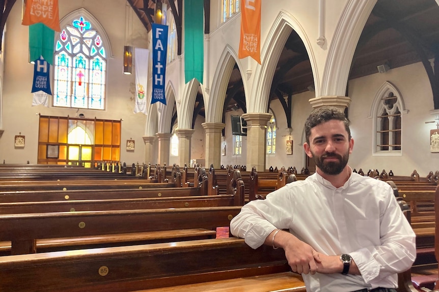 Father Nathan Webb sits in a pew in the Toowoomba Cathedral. 