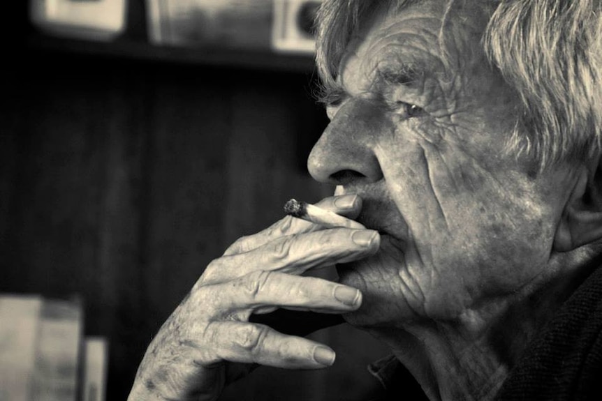 A black and white photo of an old man smoking a cigarette