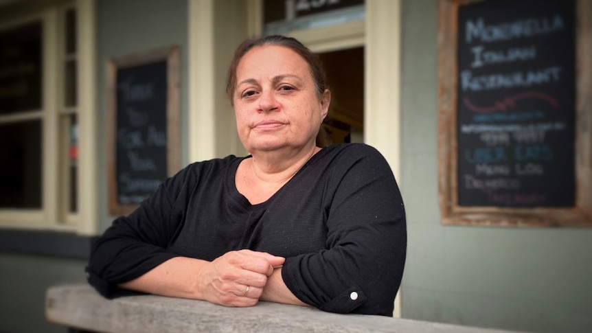 Brigitte Fava stands outside her restaurant in a black top.