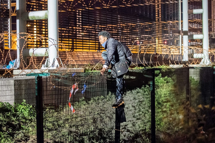 A migrant climbs a security fence of a Eurotunnel terminal near Calais