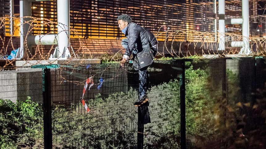 A migrant climbs a security fence of a Eurotunnel terminal near Calais