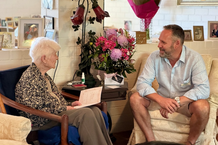 An elderly woman and a middle-aged man sit chatting in a living room.