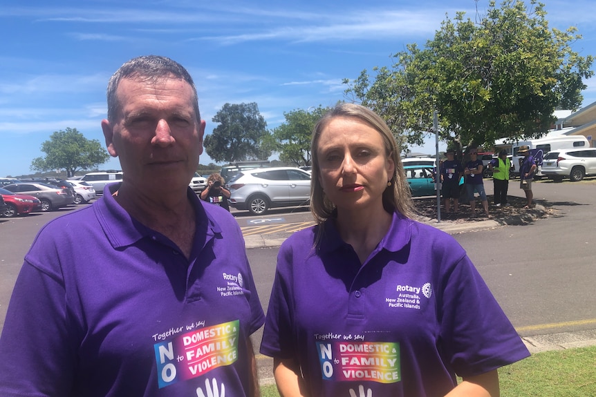 man and women in matching purple shirts standing near a carpark