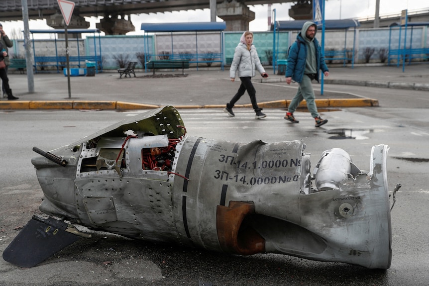 People walk past the remains of a missile at a bus terminal.