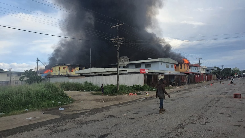 A man walks down an empty Honiara street with smoke billowing from a building