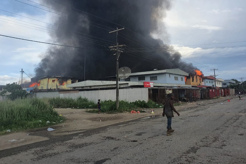 A man walks down an empty Honiara street with smoke billowing from a building