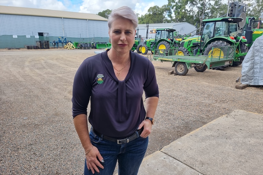 A woman with short blonde hair stands in front of tractors