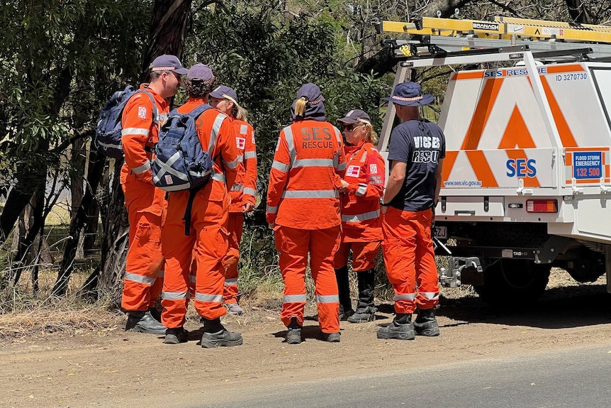 SES volunteers wearing orange uniforms in a huddle next to an SES vehicle.
