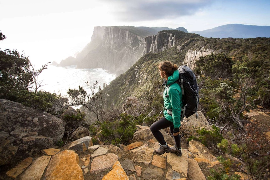 Unidentified female backpacker looks out to sea from rugged coastline.