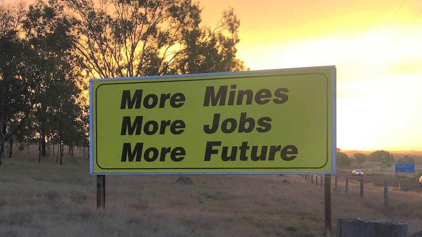 A billboard standing on the edge of a highway with the sunsetting in the background.