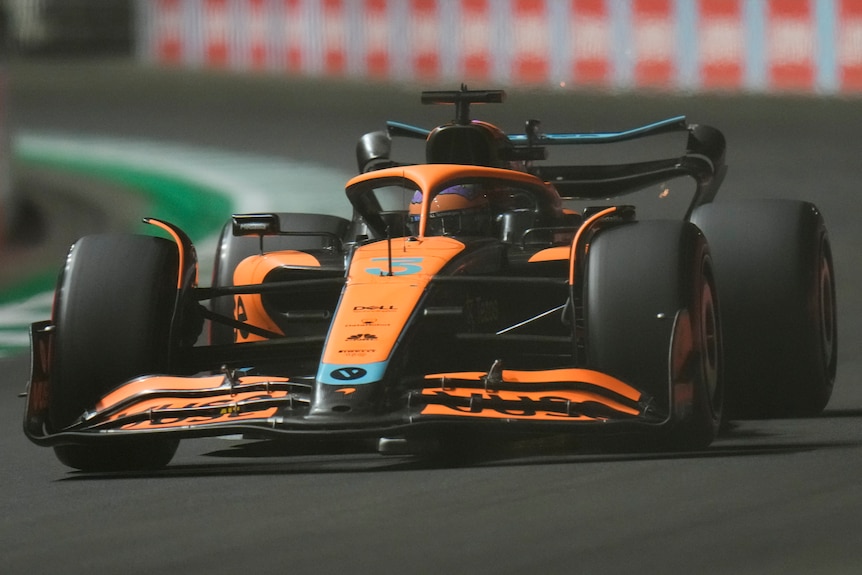 Orange F1 car driving along a street track. 