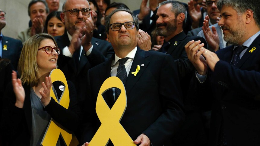 Quim Torra, centre, holds a yellow ribbon. He is surrounded by people who are clapping.