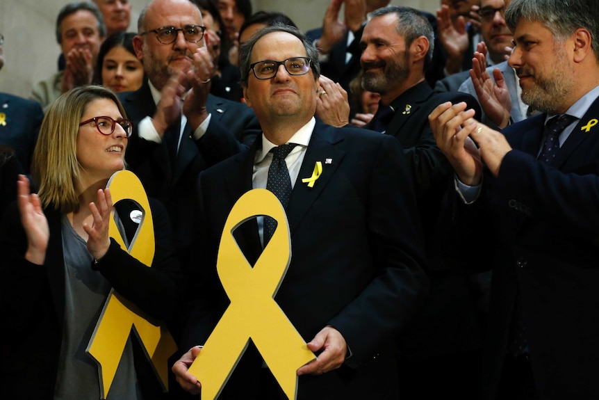 Quim Torra, centre, holds a yellow ribbon. He is surrounded by people who are clapping.