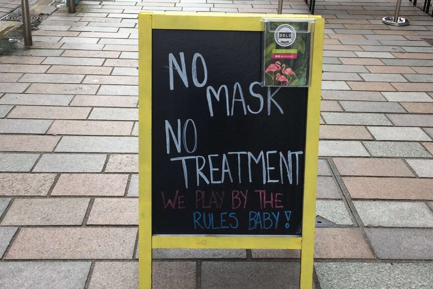 A board on a pavement saying "No Mask, no treatment"