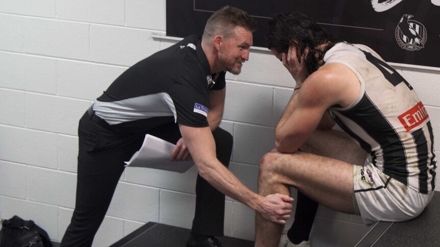 A coach talks to his player in a football changeroom.