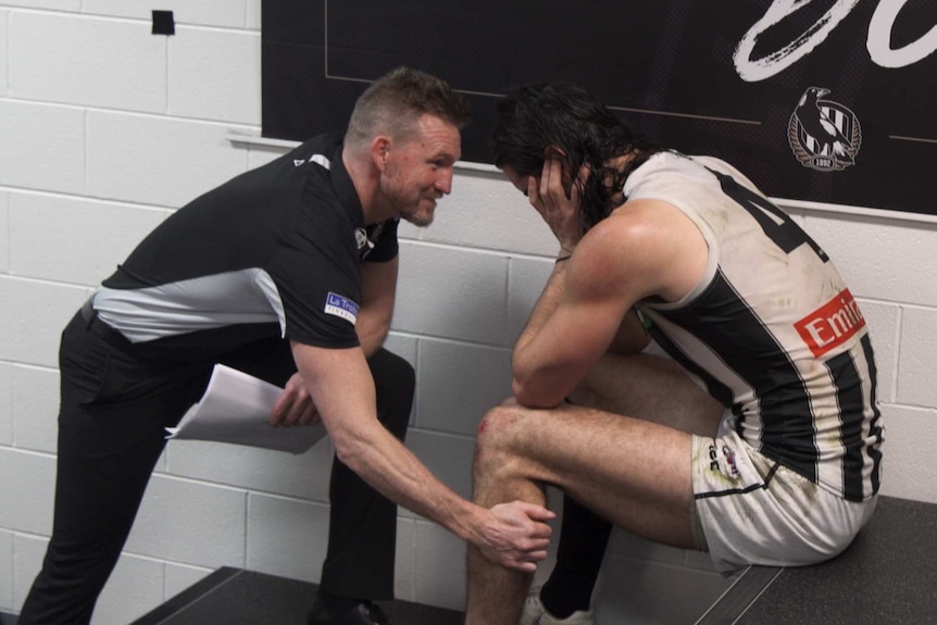 A coach talks to his player in a football changeroom.