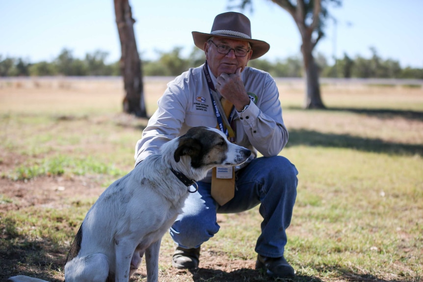 A man, Colin Koch, kneeling beside his working dog.