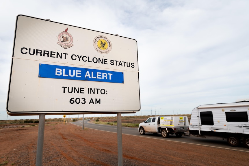 A blue alert sign on the outskirts of Port Hedland, with a departing caravan in the background.