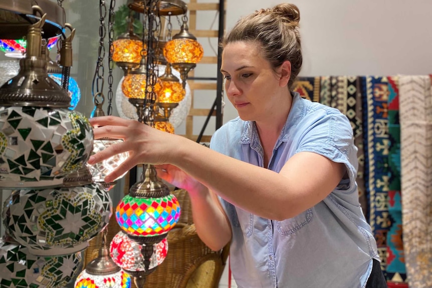 Sian tending to ornamental gifts hung by string in a gift shop.