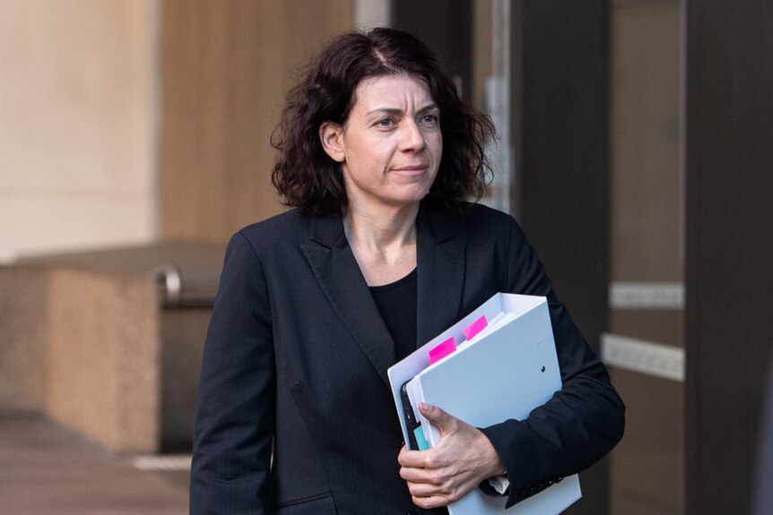 a woman holding a binder walking outside a courthouse