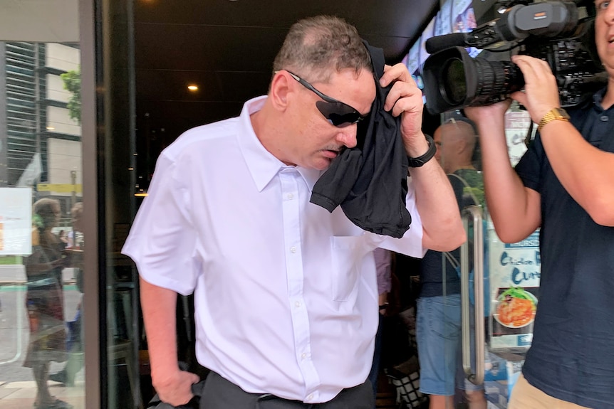 Terry Dunnett, wearing sunglasses and using a shirt to try and hide his face in Brisbane city after attending court.