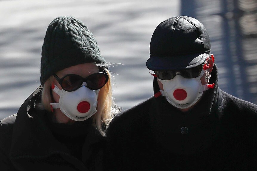 Two people wearing masks walk through a park.