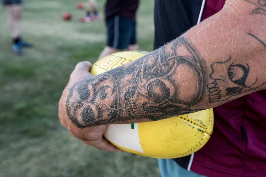 Tattooed arm holding Australian Rules football at team training, Tasmania.