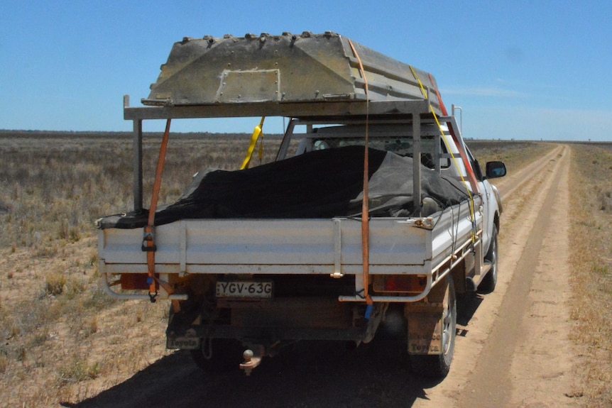 A loaded ute with something on a platform, blue sky, dirt road, no greenary.
