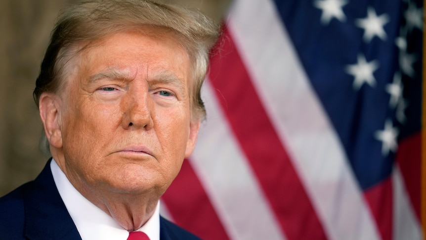 Donald Trump looks stern with US flag behind him.