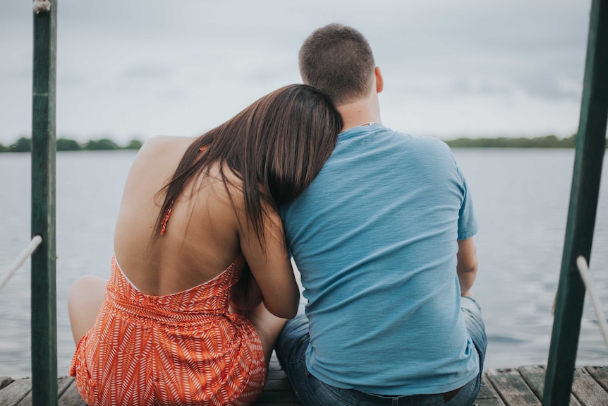 A man and woman embrace no a jetty looking at the water