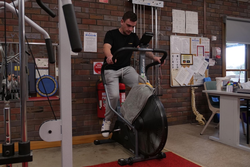 man in grey tracksuit on exercise bike in gym