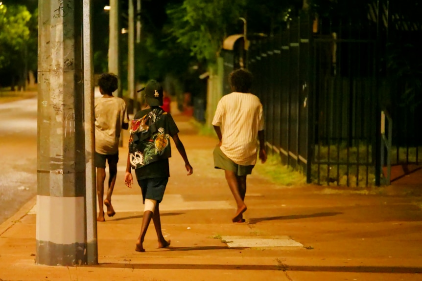 Three teenagers pictured from behind walking on a street at night