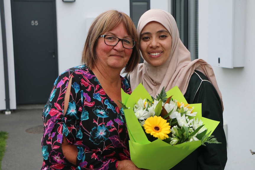 A woman in a hijab and a woman holding a bunch of flowers smile together