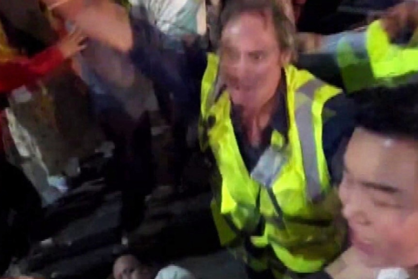 A security guard with his hand in the air above a man on the ground in a crowd