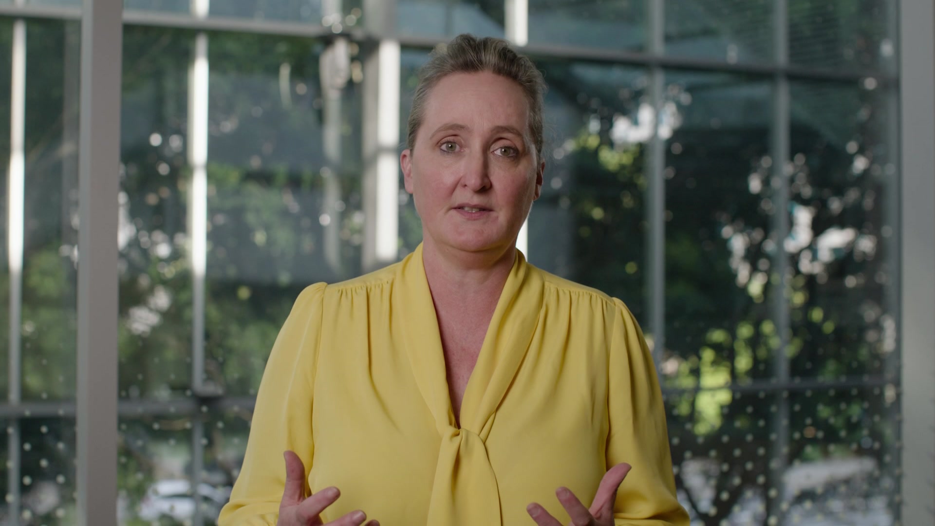 Qantas Group CEO Vanessa Hudson wearing a yellow top with trees behind her in public apology video