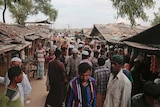 A crowd of Rohingya refugees crowd around shacks in an alley at an unregistered refugee camp.