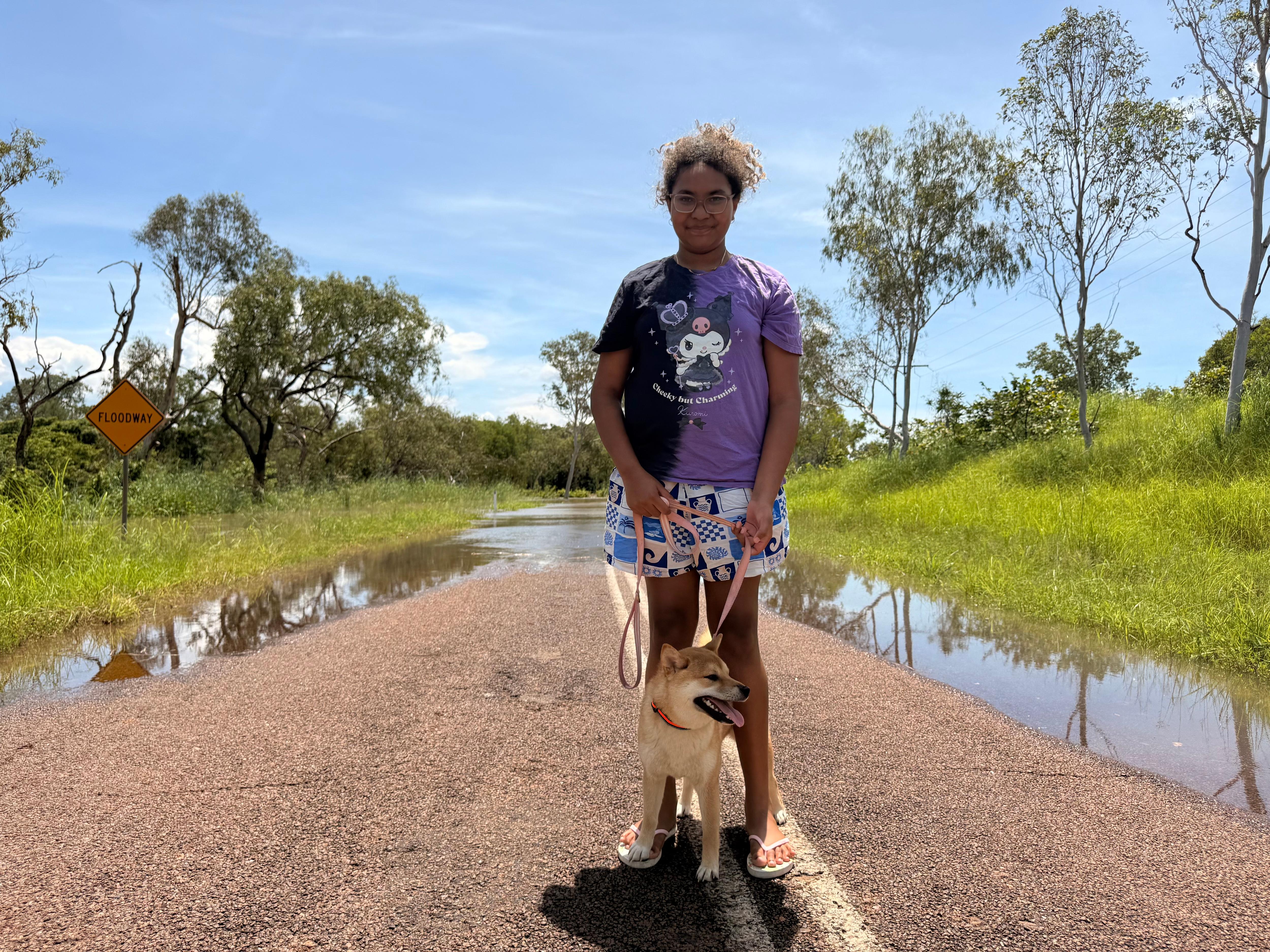 A young girl smiling, with a dog in hand in front of flooded road