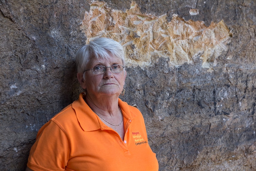 A woman stands in front of graffiti on a cave wall
