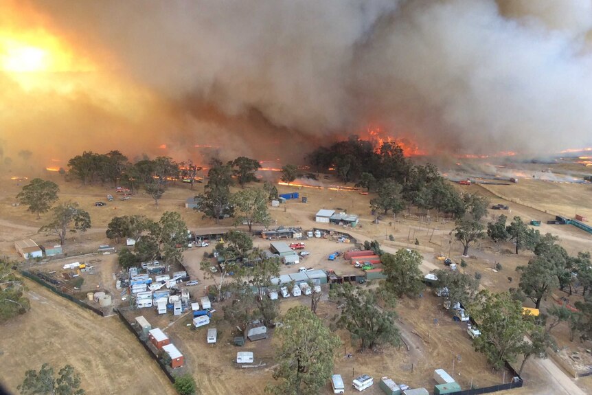 A helicopter view of a bushfire on the edge of a rural property containing dozens of shipping containers and trucks.