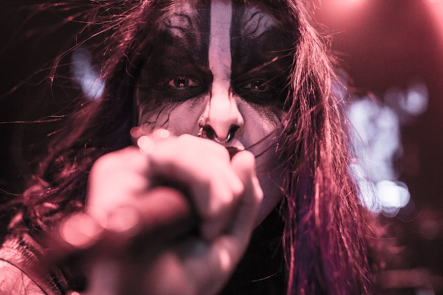 Performer wearing makeup shouting into microphone.