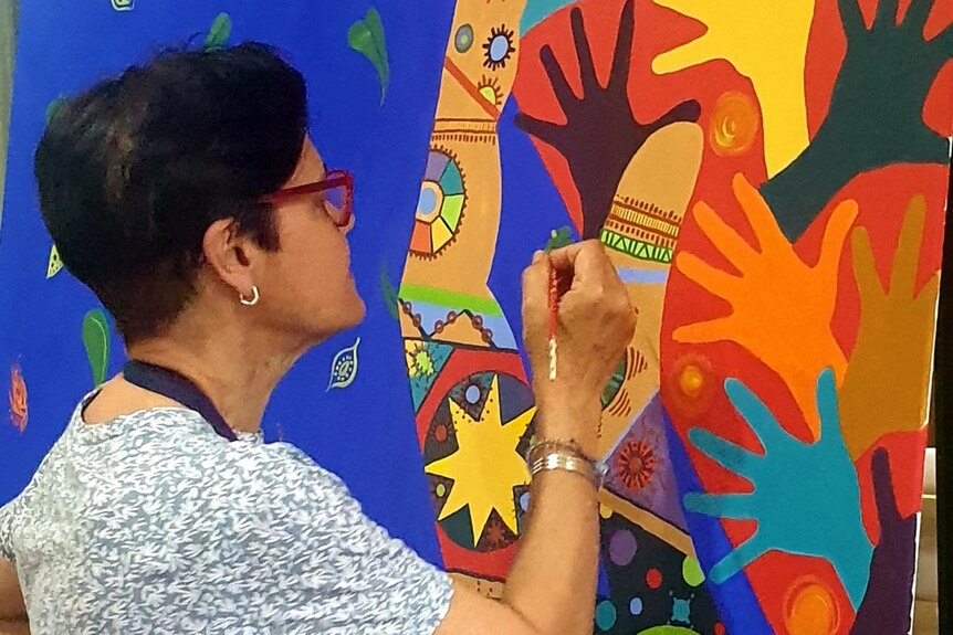 A woman paints a large coloured mural featured coloured hands.