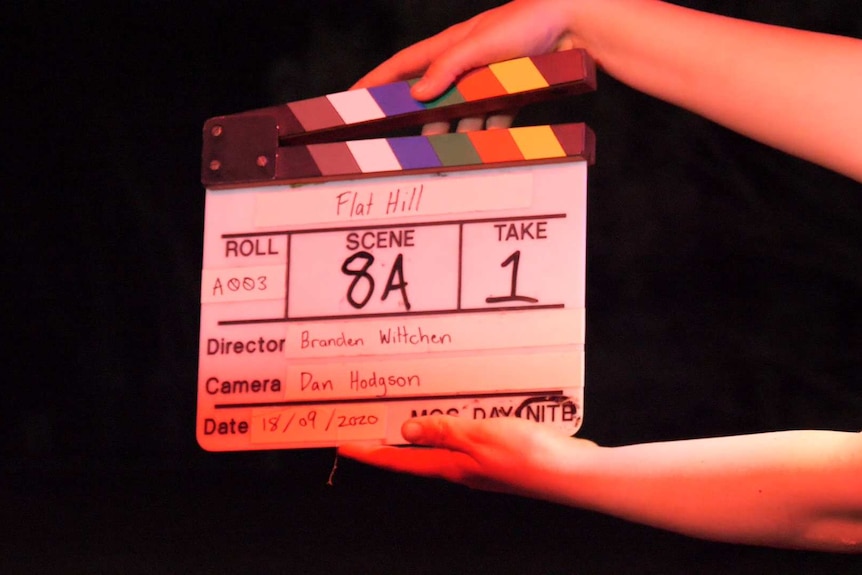A close-up shot of two hands holding a film clapperboard just before action is called on a film set.