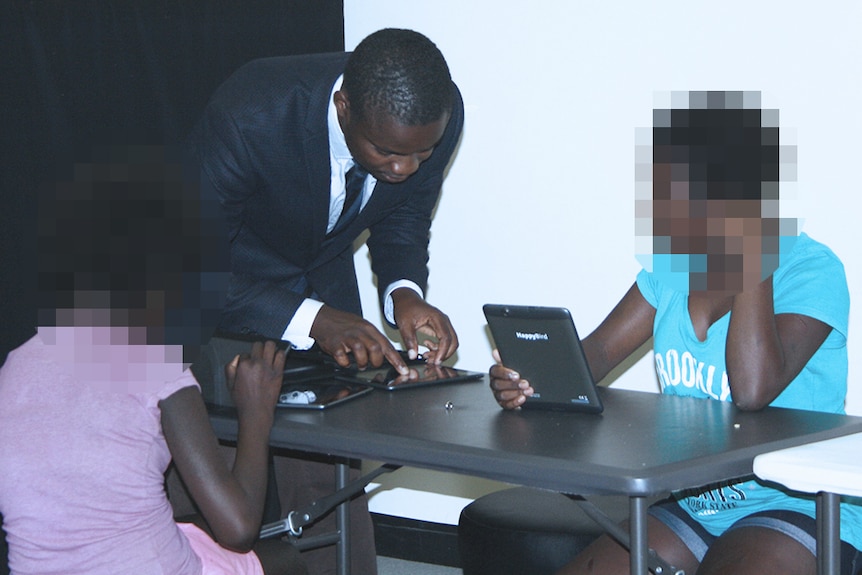 Jackson Anni, dressed in a suit, works on a tablet device with two Indigenous women beside him.